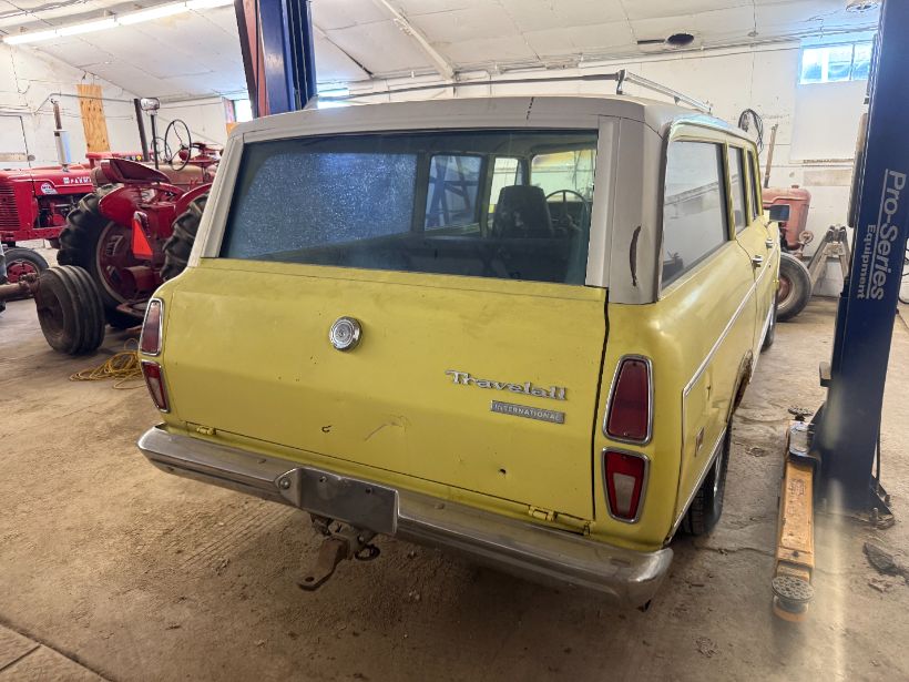 Yellow International Travelall station wagon parked among red tractors